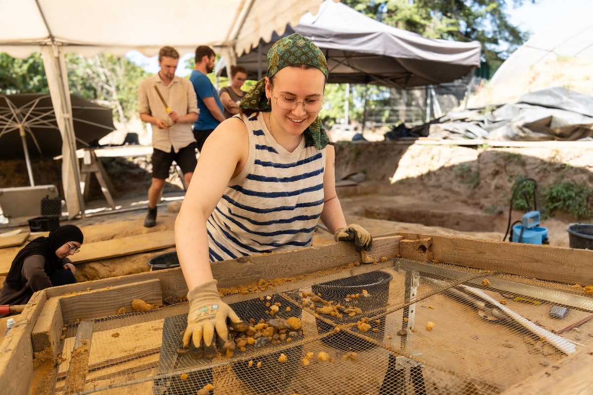 Studentin siebt bei der archäologischen Ausgrabung Erde