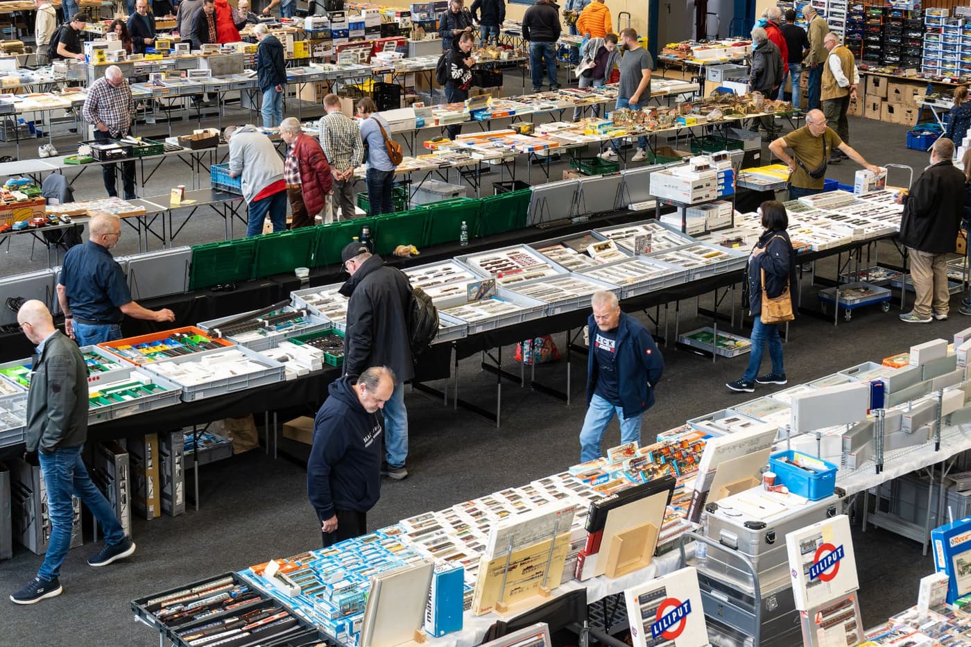 Besucher gehen zwischen Verkaufstischen mit Modellspielzeug in der Seestadthalle