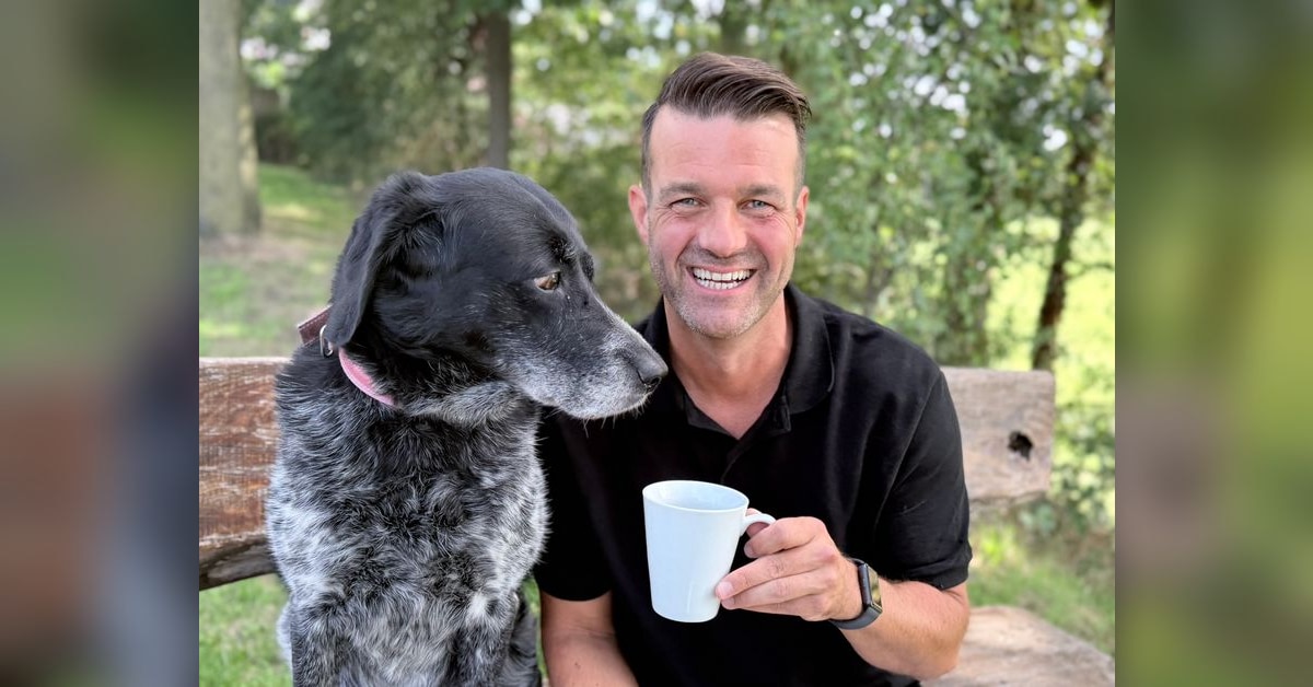 Michael Keller sitzt mit seinem Hund auf einer Bank und hält eine Kaffeetasse