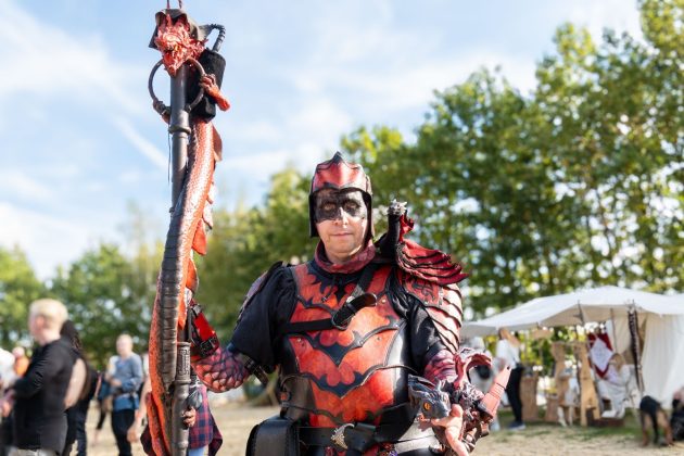 Rot-schwarze Fantasyr&uuml;stung und ein verzierter Stab fallen zwischen den Besuchern auf